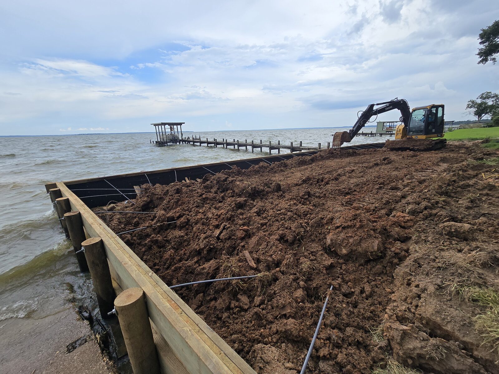 Barge-mounted excavator setting a steel sheet-pile bulkhead along a Texas shoreline